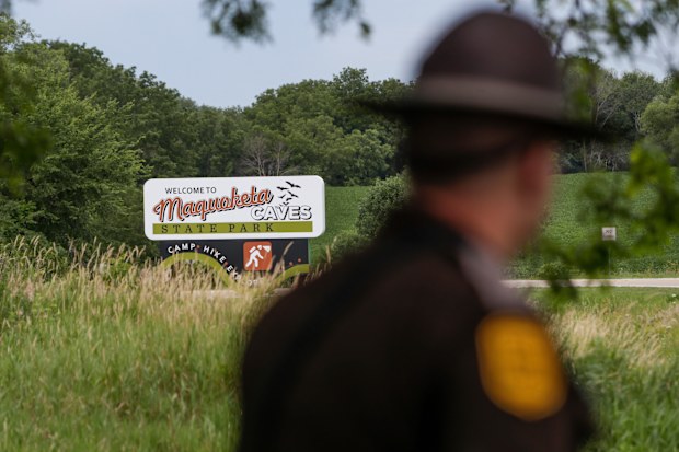 An Iowa State Patrolman walks past a Maquoketa Caves State Park sign as police investigate a shooting that left several people dead, Friday, July 22, 2022, in Maquoketa, Iowa. 