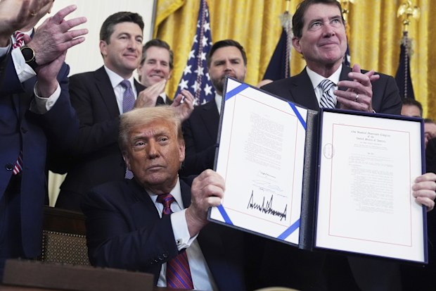 President Donald Trump holds up the signed document after signing the GENIUS Act