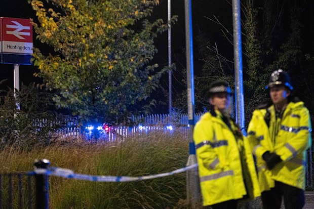 Police officers stand near a cordon outside Huntingdon Station  where the train stopped after the attack
