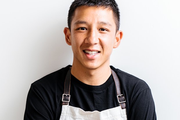 Brendan Pang poses in a black shirt and white apron