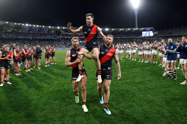GEELONG, AUSTRALIA - JULY 15: Zach Merrett of the Bombers is chaired from the field after his 200th match by teammates Dyson Heppell (left) and Jake Stringer (right) during the 2023 AFL Round 18 match between the Geelong Cats and the Essendon Bombers at GMHBA Stadium on July 15, 2023 in Geelong, Australia. (Photo by Michael Willson/AFL Photos via Getty Images)