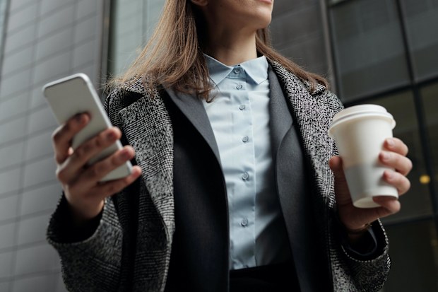 Stock photo of a successful business woman holding phone and coffee.