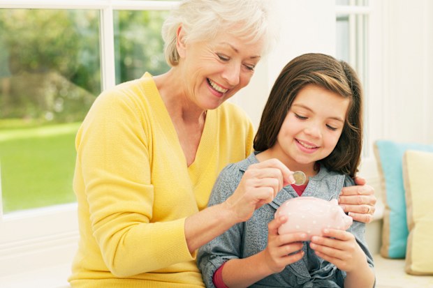 Grandmother putting coin into granddaughters piggy bank - stock photo