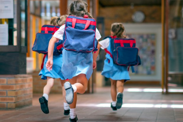 Rear view of excited students running towards entrance. Girls are carrying backpacks while leaving from school. Happy friends are wearing school uniforms.