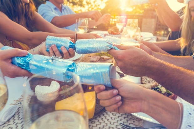 Group of people with Christmas crackers. There is food on the table outdoors in a December Summer. There is Cheese and wine. Could be a family. Low angle view.