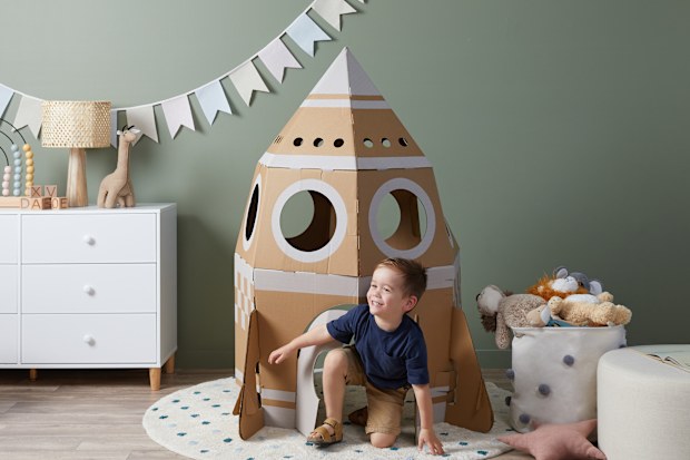 Boy playing inside carboard rocket ship.