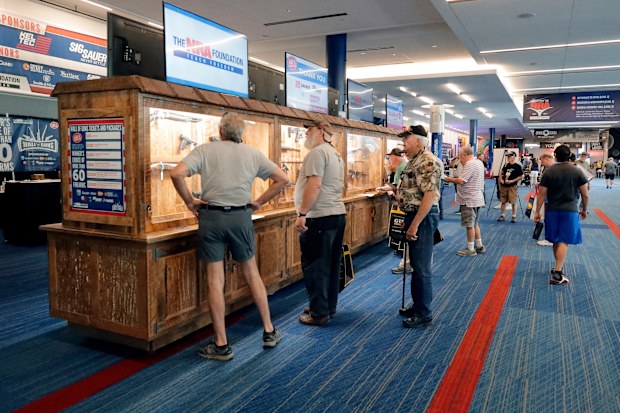 Convention attendees look at various rifles and handguns in display cases that are being raffled off at the Gallery of Guns booth at the NRA Annual Meeting at the George R. Brown Convention Center Thursday, May 26, 2022, in Houston. (AP Photo/Michael Wyke)