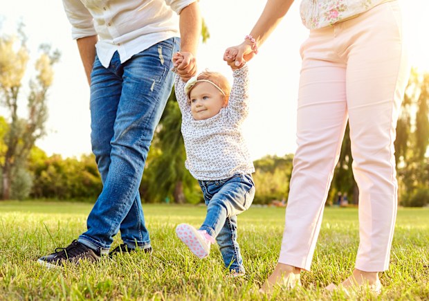 The first steps of the baby. Parents are teaching their child to walk. A happy family.