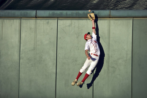 A baseball player leaps for a catch against the padded boundary wall.