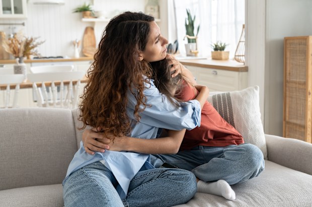 Caring loving mother comforting hugging unhappy sad teenage daughter, sitting together on sofa at home, mom supporting depressed teen girl child, parent making peace with kid. Parenting of adolescents
