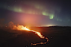 A view of the lava flowing from the volcano backdropped by the Northern Lights, near the town of Grindavik, Iceland, early Saturday, March 23, 2024.  The volcano in southwestern Iceland that erupted three times in December, January and February, sending lava towards a nearby community, keeps erupting. (AP Photo/Marco di Marco)