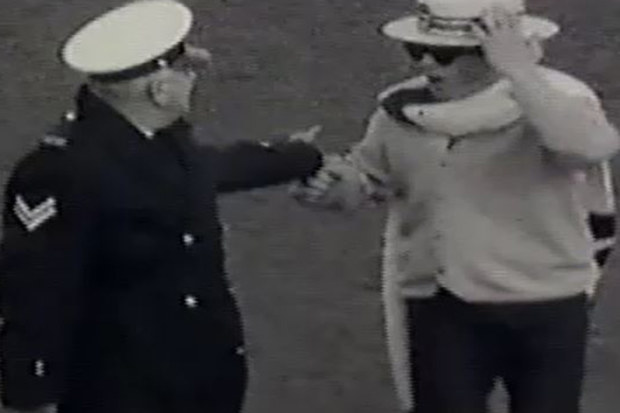 Molly Meldrum is escorted off the ground by a police sergeant.