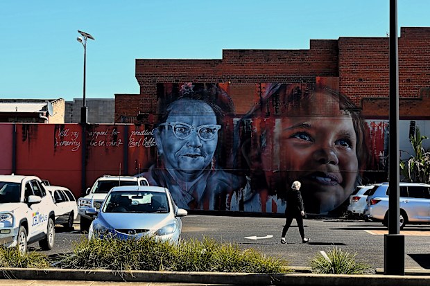 A woman walks across a car park in front of a mural on the side of a building on Talbragar Street in Dubbo, NSW. (Photo: Kate Geraghty)