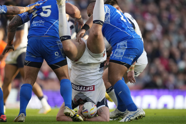 England's Tom Burgess, falls on the ground after a tackle by Samoa's Royce Hunt and captain Junior Paulo during the Rugby League World Cup semi-final match between England and Samoa at Emirates Stadium, London, England, Saturday, Nov. 12, 2022. (AP Photo/Frank Augstein)