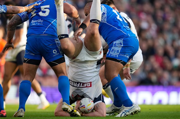England's Tom Burgess, falls on the ground after a tackle by Samoa's Royce Hunt and captain Junior Paulo during the Rugby League World Cup semi-final match between England and Samoa at Emirates Stadium, London, England, Saturday, Nov. 12, 2022. (AP Photo/Frank Augstein)