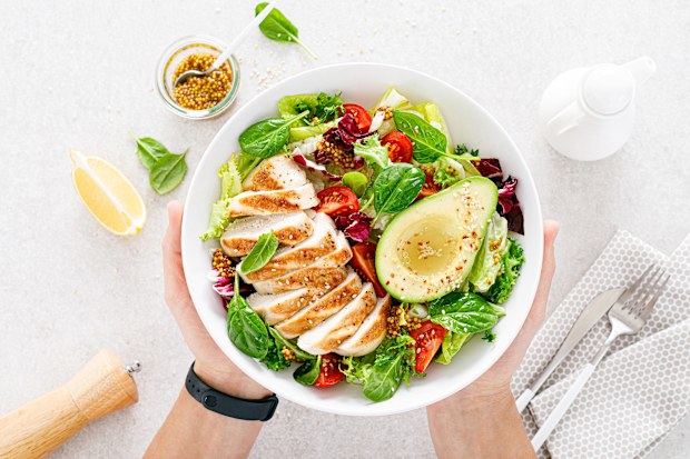 Grilled chicken meat and fresh vegetable salad of tomato, avocado, lettuce and spinach. Healthy and detox food concept. Ketogenic diet. Buddha bowl in hands on white background, top view