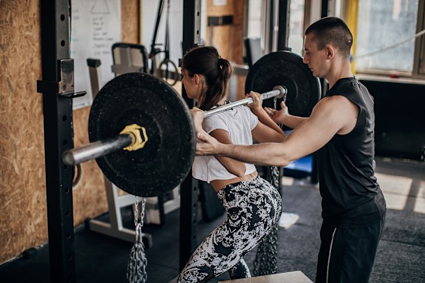 Two people, man and woman, male personal trainer assisting a woman in weight training in gym.