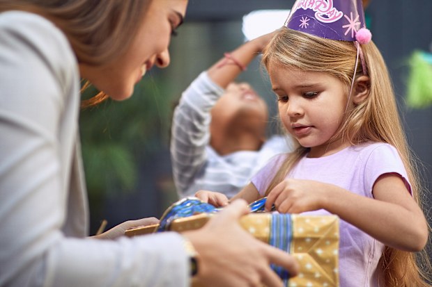 little girl unwrapping birthday present from young adult female brunette