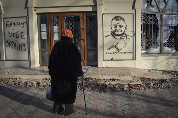 An elderly woman looks at a graffiti depicting General Valery Zaluzhny, head of Ukraine's armed forces and writing "God is with us and commander Zaluzhny" in the site of the heaviest battles with the Russian invaders in Bakhmut, Ukraine, Tuesday, December 20, 2022