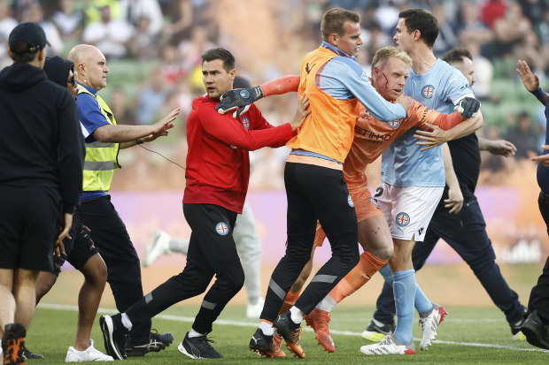 A bleeding Tom Glover of Melbourne City is escorted from the pitch by team mates after fans stormed the pitch during the round eight A-League Men's match between Melbourne City and Melbourne Victory.