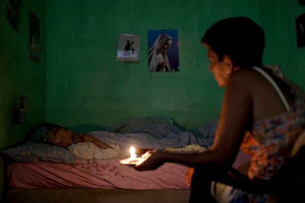 A woman sits beside her sick mother holding a candle. She says the hours of intermittent electricity supply in Venezuela affects her capacity to care for, bathe and feed her mother.