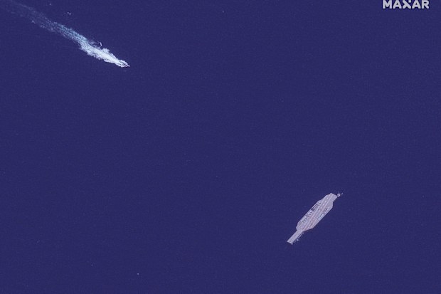 An Iranian fast boat, top left, approaches a mock-up aircraft carrier built by Iran, in the Strait of Hormuz.