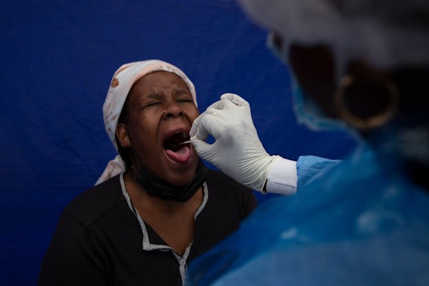 A throat swab is taken from a patient to test for COVID-19 at a facility in Soweto, South Africa, Wednesday Dec. 2, 2021.  
