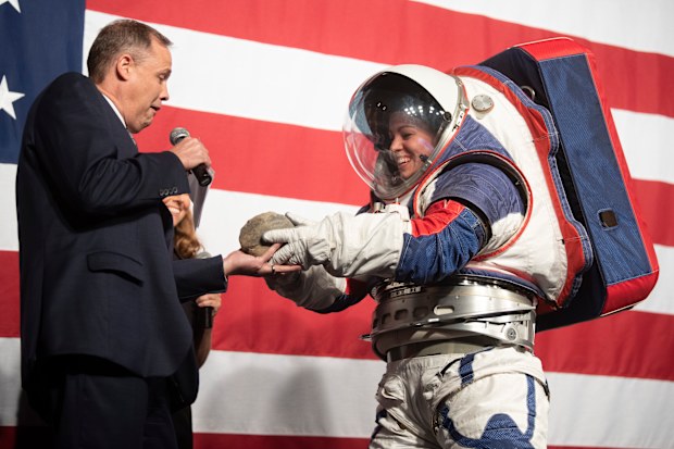 Kristine Dans hands a rock to NASA administrator Jim Bridenstine during a demonstration of the Exploration Extravehicular Mobility Unit (xEMU), one of two NASA spacesuit prototypes for lunar exploration on Tuesday, Oct. 15, 2019, at NASA Headquarters in Washington. 