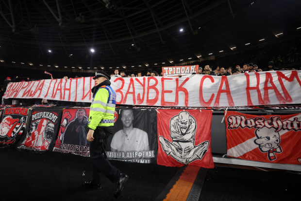 A police officer walks past as Olympiakos fans hold up a banner.