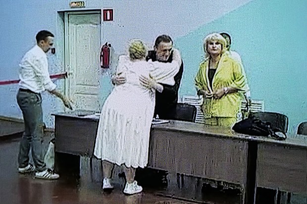 Russian opposition leader Alexei Navalny is seen on a TV screen embracing a lawyer, as he appears in a video link provided by the Russian Federal Penitentiary Service, during a hearing in the colony, in Melekhovo, Vladimir region, about 260 kilometres northeast of Moscow, Russia, on Friday, Aug. 4, 2023.  