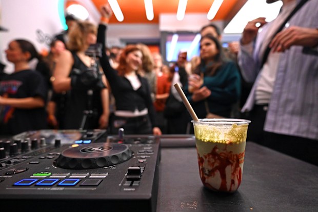 A plastic cup filled with matcha latte stands next to a DJ booth. Dancing young people can be seen in the background. At the "Coffee Rave" event, partygoers in Berlin can dance to electronic music in the morning. Only non-alcoholic drinks are sold in the café. According to the organizer, many young people are looking for party alternatives in order to celebrate in a healthy way. Photo: Elisa Schu/dpa 