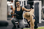 A female personal trainer is training sportswoman in a gym and tracking her progress on a a tablet.