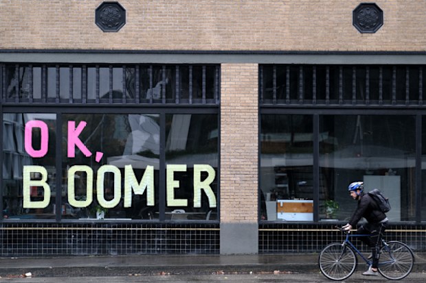 A man bikes past sticky notes arranged to display the phrase "OK Boomer" in a window of a business in Portland, Oregon.