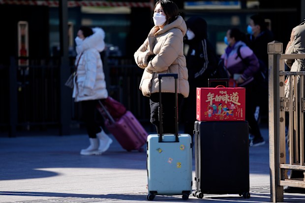 A traveller waits outside the Beijing Station with her trolley bags and a gift box with the words The taste of New Year in Beijing, China, Friday, Jan. 28, 2022. 
