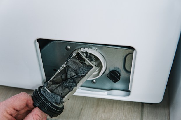 Male hand removes dirty and clogged washing machine pump filter