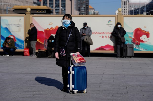 A traveller waits outside the Beijing Station with her suit case in Beijing, China, Friday, Jan. 28, 2022. 