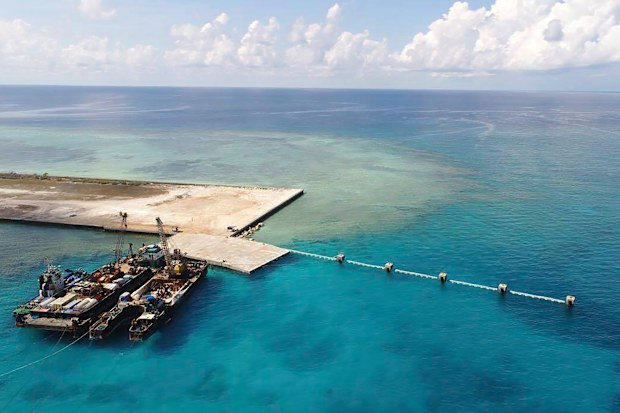 In this photo provided by the Department of National Defense, ships carrying construction materials are docked at the newly built beach ramp at the Philippine-claimed island of Thitu, in the disputed South China Sea, June 9, 2020.