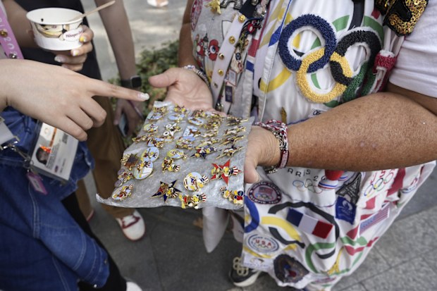Vivianne Robinson lets a passer by choose one of the pins Robinson collected from USA Olympics 1984, during 2024 Summer Olympics, in Paris, France, Tuesday, July 30, 2024. The Olympics superfan has attended seven Games over the span of 40 years. (AP Photo/Lujain Jo)