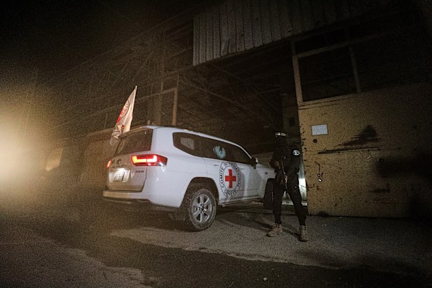 A gunman wearing the uniform of the al-Qassam Brigades, the military wing of Hamas, stands guard as Red Cross vehicles enter a warehouse allegedly to collect coffins containing the bodies of four deceased hostages, in Gaza.