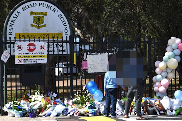 A father holds the hand of his son as they look at tributes laid outside the main entrance to Banksia Road Public School in Greenacre, Sydney, on November 8, 2017.