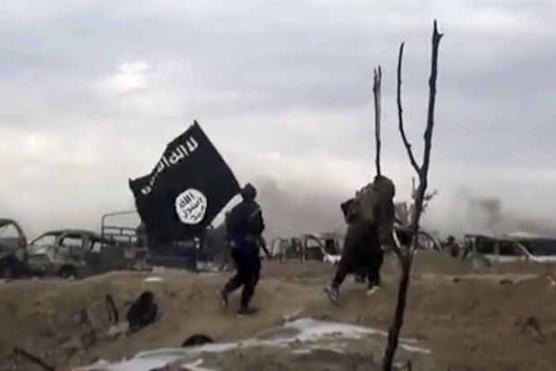 IS fighters walk as they hold the group's flag inside Baghouz in Syria. 