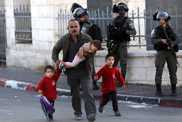 A Palestinian man and children walk past Israeli soldiers during an anti-Israel protest by Palestinians in the West Bank city of Bethlehem.
