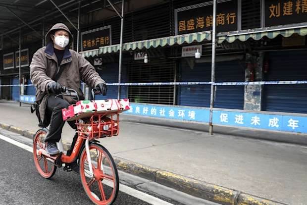 A man wears a mask while riding on mobike past the closed Huanan Seafood Wholesale Market, which has been linked to cases of coronavirus.