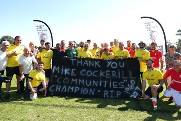 Participants in the 2025 Mike Cockerill Cup hold up a sign in tribute to the man they are there in honour of.