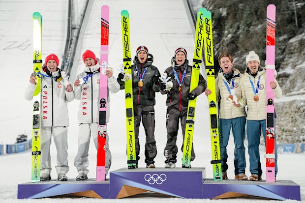Gold medalists Stephan Embacher and Jan Hoerl, of Austria, celebrate on the podium, with silver medalists Pawel Wasek and Kacper Tomasiak, of Poland, and bronze medalists Kristoffer Eriksen Sundal and Johann Andre Forfang, of Norway, after the ski jumping men's super team competition at the 2026 Winter Olympics, in Predazzo, Italy, Monday, Feb. 16, 2026. (AP Photo/Evgeniy Maloletka)