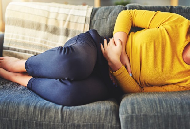 Cropped shot of a woman suffering from stomach cramps on the sofa at home