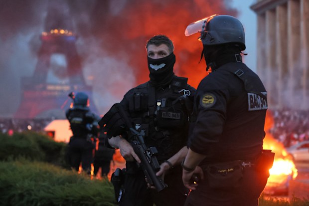 A car burns and fireworks explode as police watch PSG supporters celebrate in Paris.