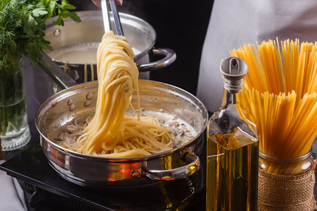 young woman in a gray apron preparing pasta.