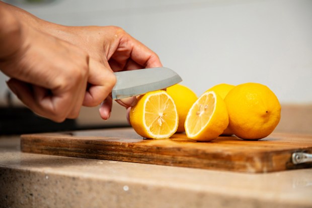 The woman is cutting the yellow lemon with a knife