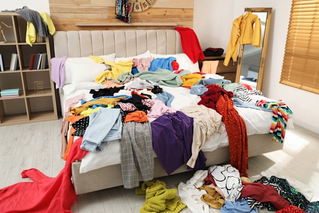 Pile of clothes on bed in messy room. 